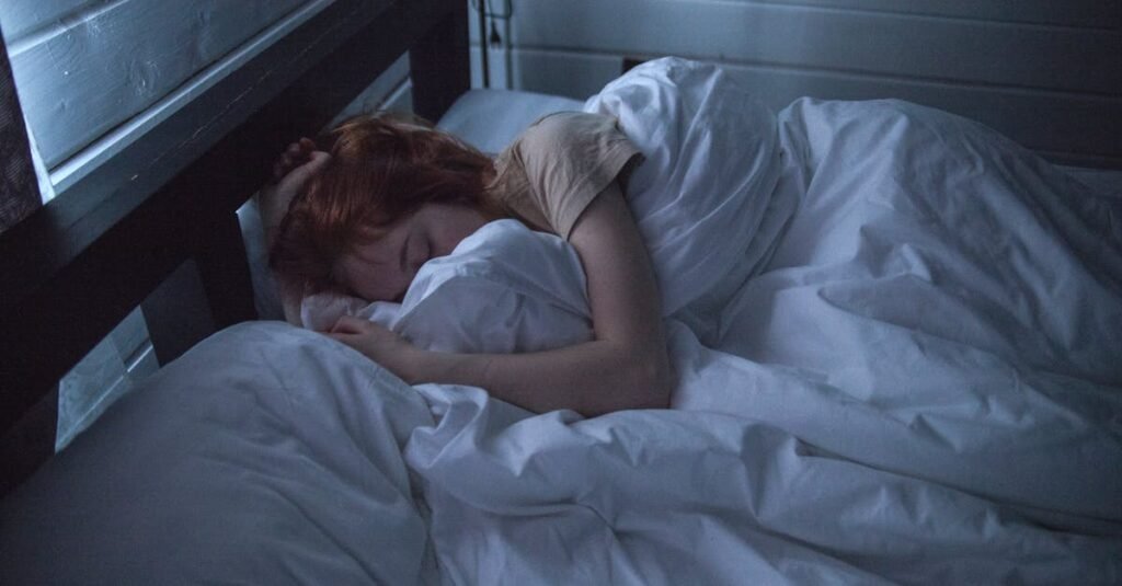 A woman sleeping peacefully in a cozy bedroom, enveloped by soft white sheets, under the gentle glow of night lighting.